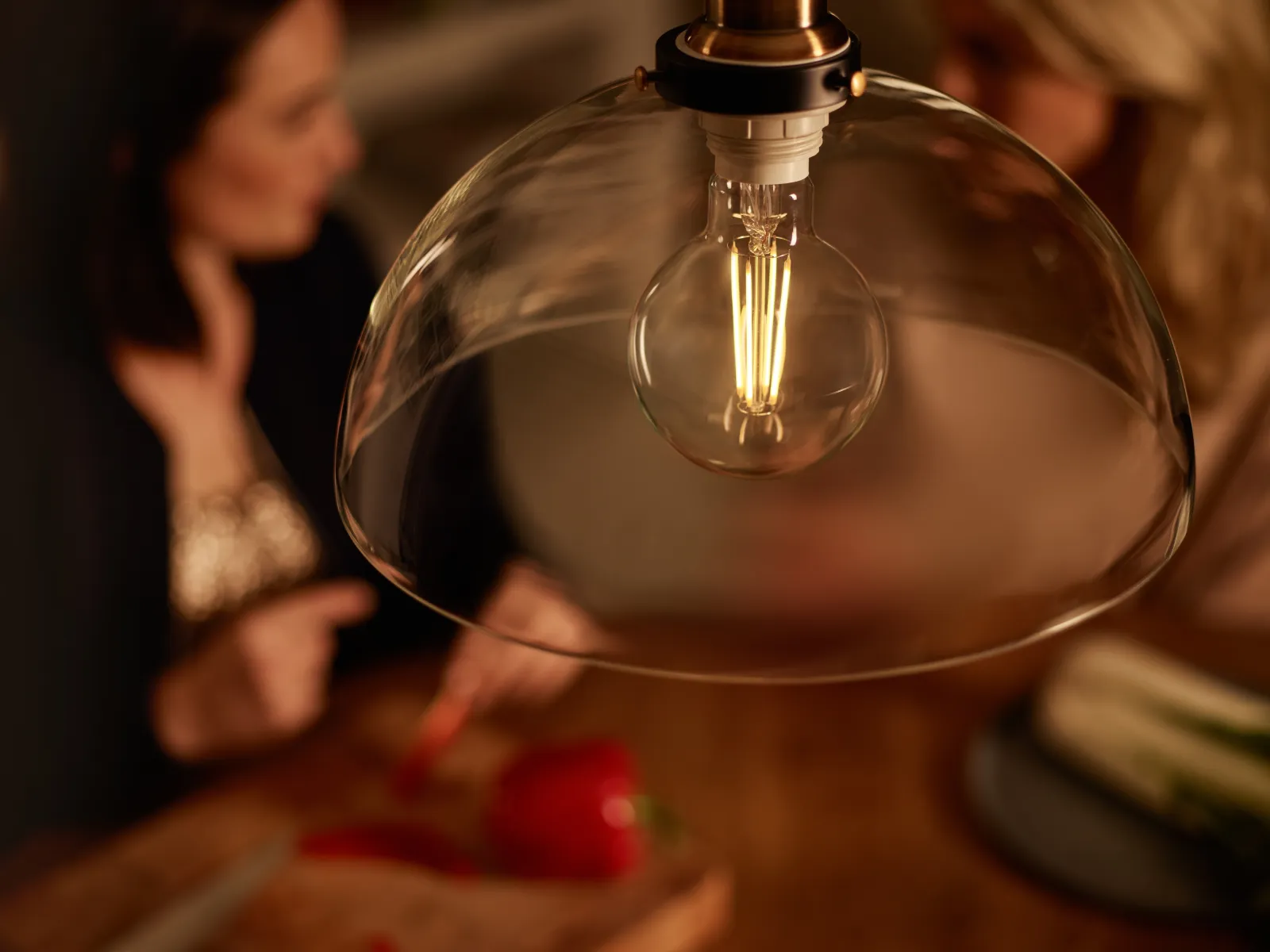 A lit Philips LED filament bulb under a broad glass lamp shade